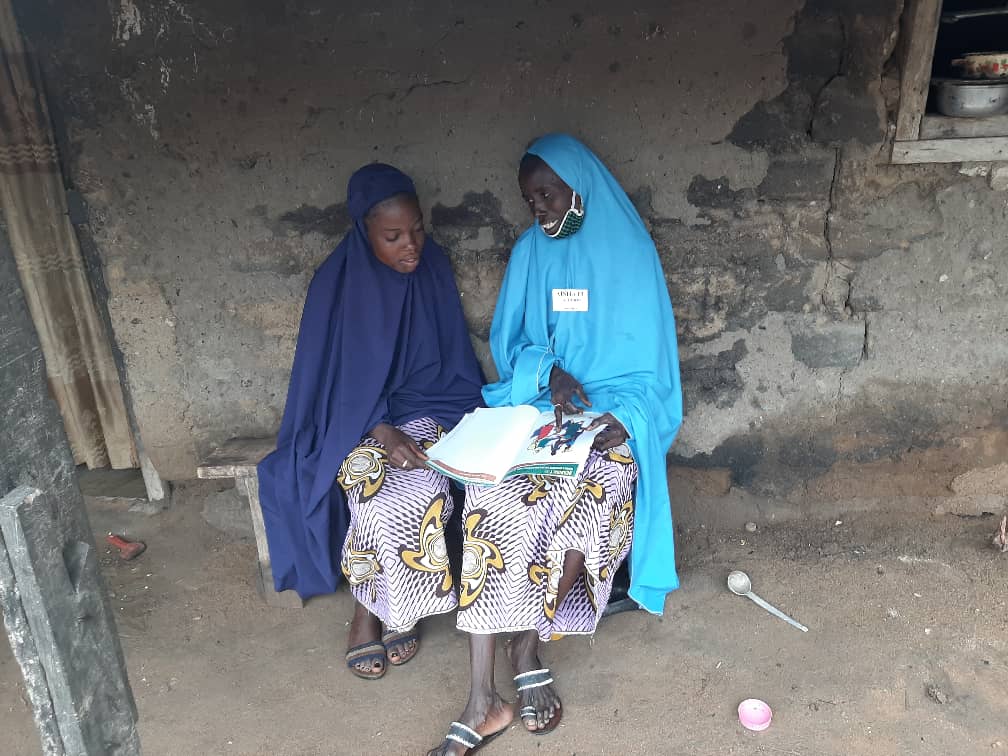 Aishatu sits with her daughter, Ummi, on a bench as they go through the Women for Women International handbook